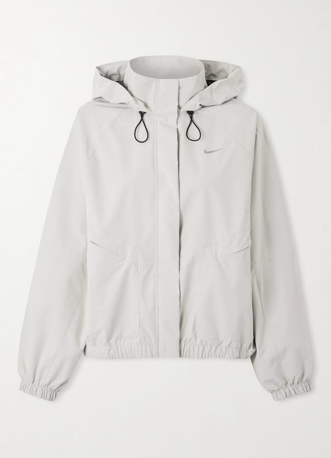 A light grey hooded jacket with a front zip, two side pockets, elasticated cuffs and hem, and a subtle Nike logo on the chest. Black drawcords on the hood add style to this piece from the latest activewear collection.