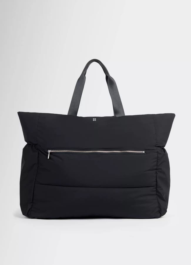 A large black puffer tote bag with two short handles and a front zipped pocket, perfect for carrying your latest activewear, set against a plain light grey background.