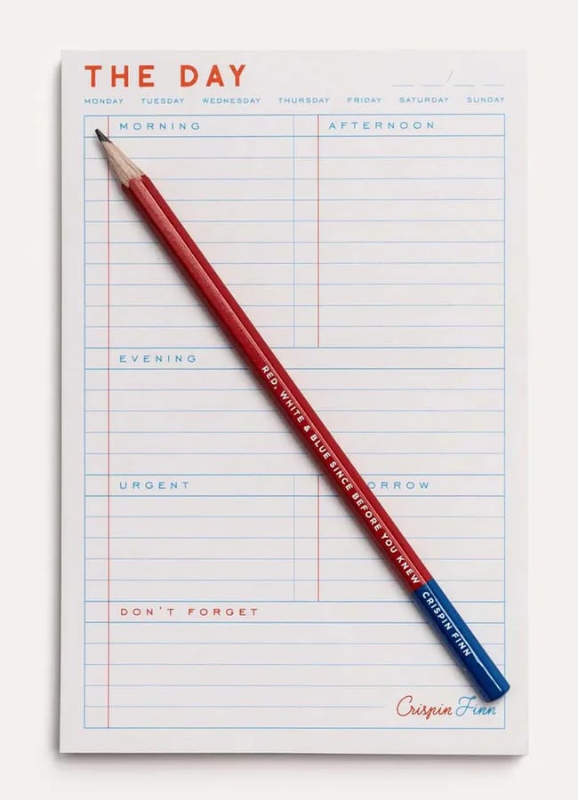 A notepad titled THE DAY with sections for morning, afternoon, evening, urgent, and don't forget. A red and blue pencil lies diagonally across the notepad—perfect for planning alongside your 2026 diaries.