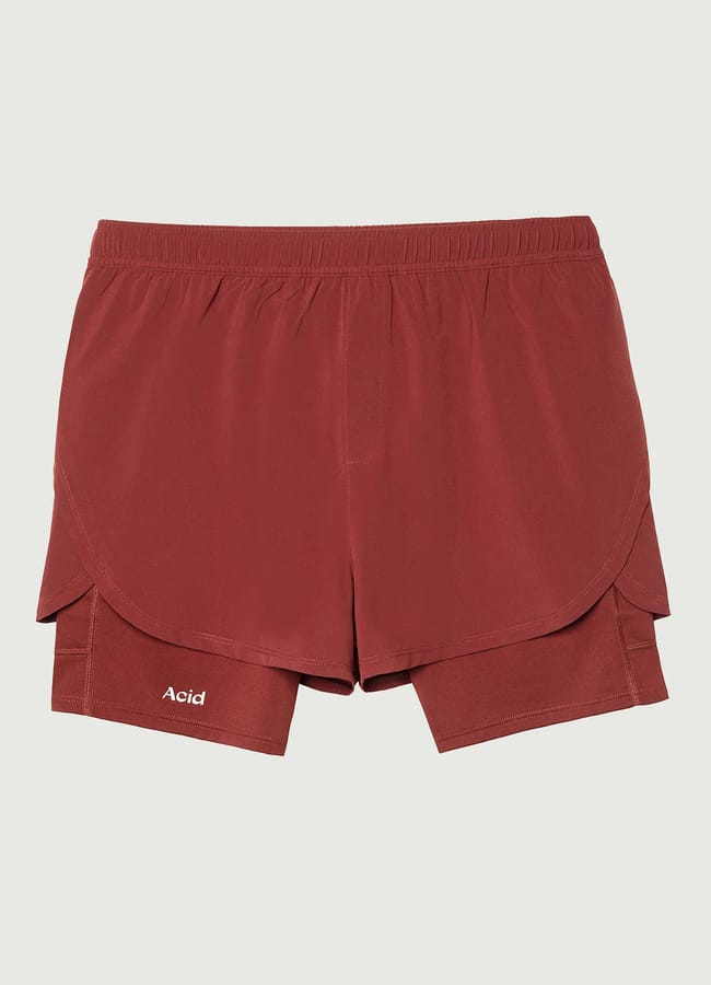 Red athletic shorts with an elasticated waistband and inner compression lining, perfect as gym wear for men, featuring the word Acid printed in white on the left leg. The shorts are laid flat on a light background.