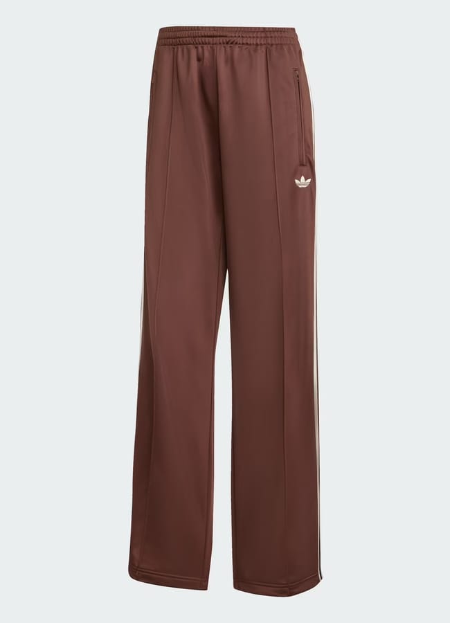 A pair of brown Adidas track bottoms with a relaxed fit, elasticated waistband, side pockets, and the classic white Adidas Trefoil logo on the left thigh—perfect for comfortable everyday wear.
