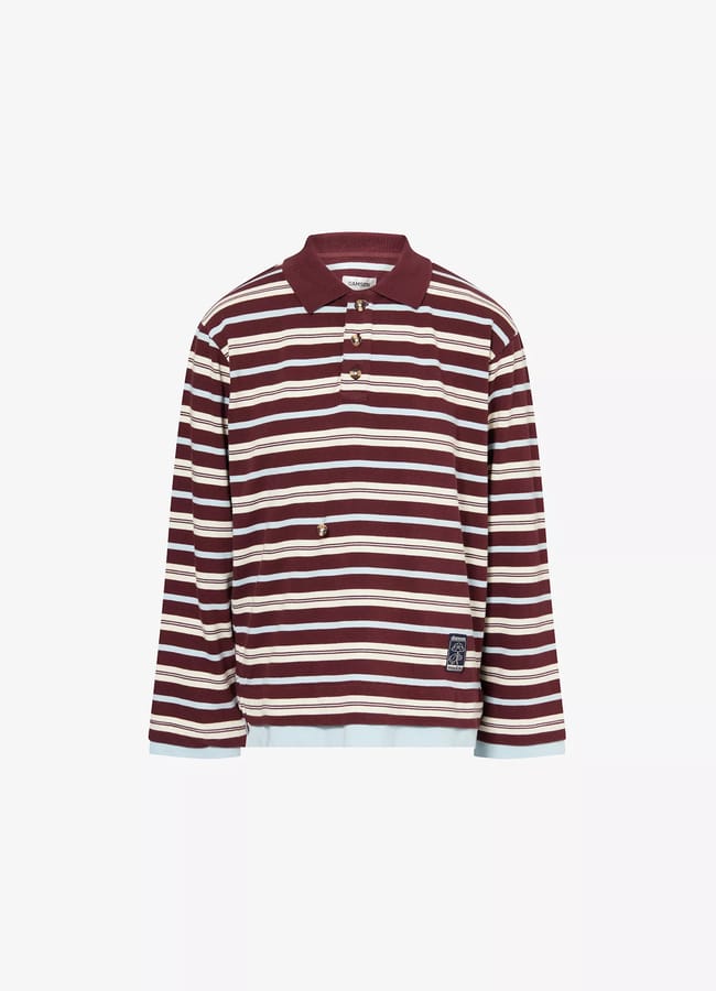A long-sleeve rugby shirt with maroon and white horizontal stripes, a maroon collar, and button placket. The relaxed fit pairs perfectly with track bottoms, and a small rectangular patch accents the hem.