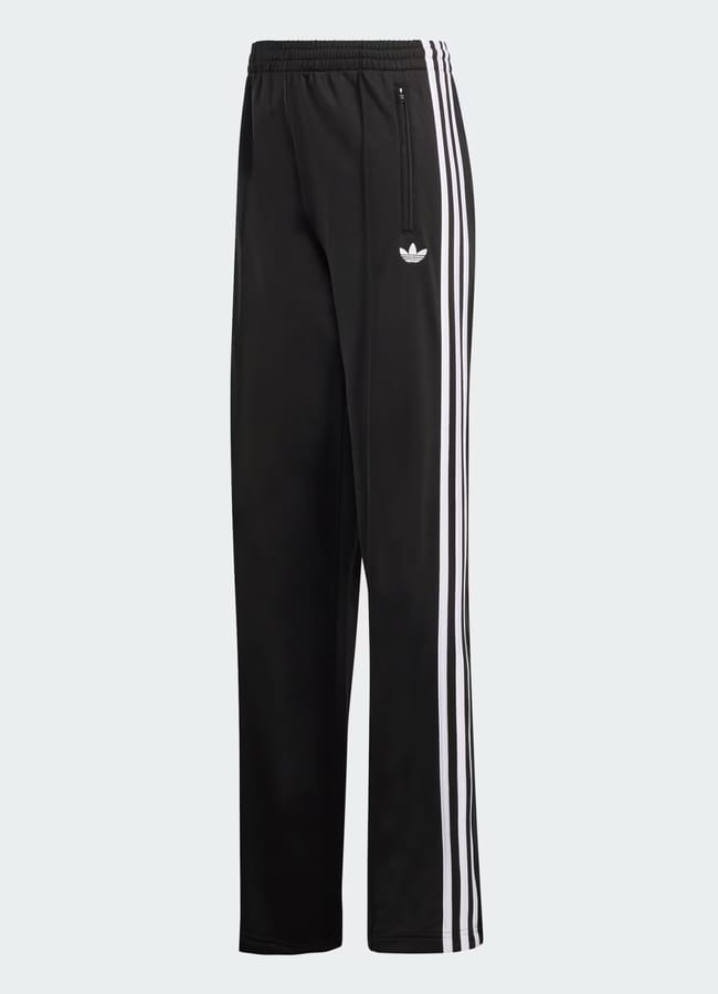 These black Adidas track trousers feature iconic white three-stripe detailing down the sides, an elasticated waistband, front zip pocket, and the Adidas Trefoil logo on the upper left thigh, displayed on a plain light background.