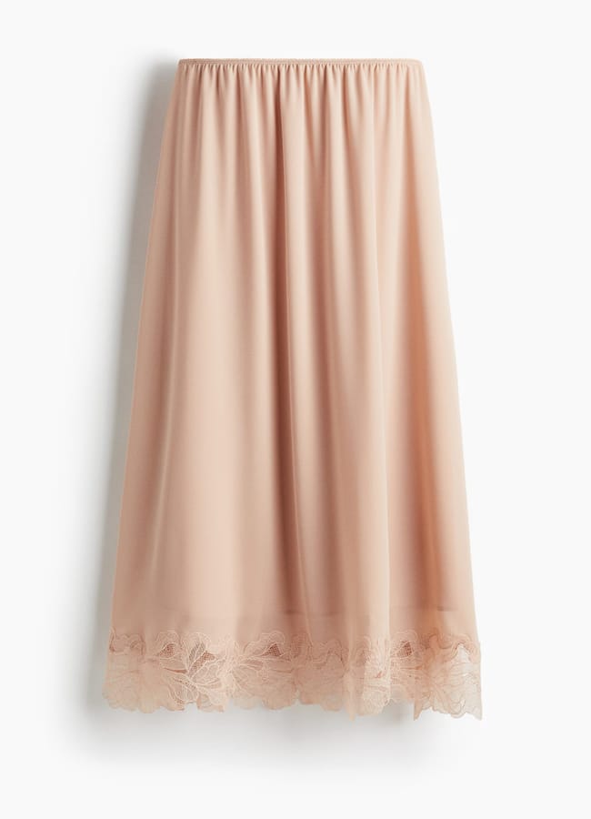 A knee-length, light pink slip skirt with an elasticated waistband and delicate lace trim along the hem—perfect for elevating your women's workwear wardrobe.