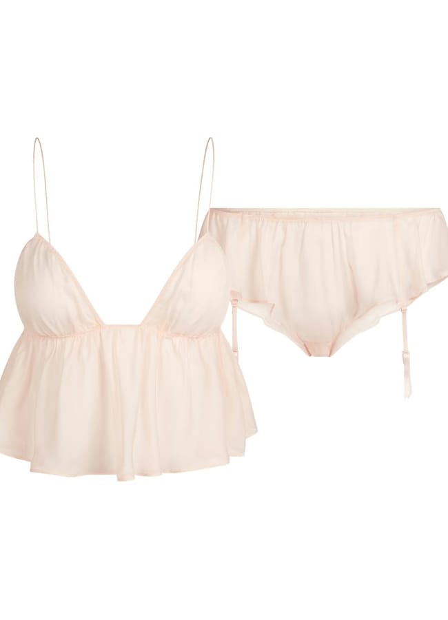A pale pink lingerie set features a sheer spaghetti strap babydoll top with a flowy, ruffled hem and matching knickers with ruffle details and detachable suspender straps, displayed on a white background.