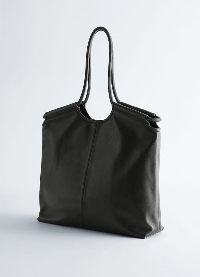 A large, black leather tote bag with thin double shoulder straps, perfect for your No-Spend January or budgeting goals, stands upright against a plain white background.