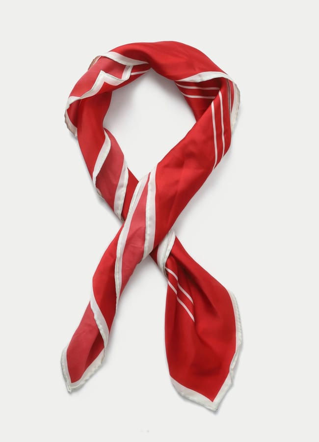 A red silk scarf with white diagonal stripes, perfect for those who love red accessories, lies arranged in a loose knot on a plain white background.