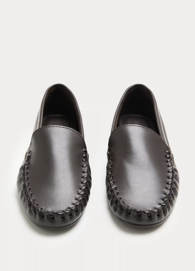 A pair of black leather slip-on loafers with visible hand-stitched detailing around the front edges, perfect for pairing with tracksuit bottoms, photographed from above on a plain white background.