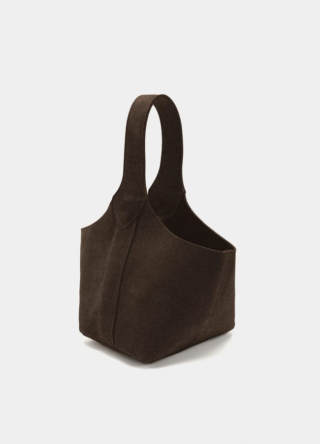 A dark brown, suede tote bag with a single thick handle is shown on a plain white background. Perfect for pairing with casual looks like tracksuit bottoms, the bag features a soft, structured shape with visible seams and an open top.