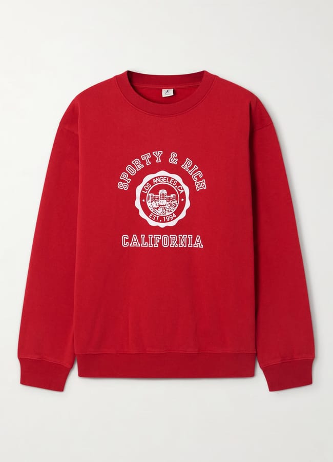 A red crewneck sweatshirt in athleisure style, featuring white printed text that reads SPORTY & RICH CALIFORNIA and a round emblem with LOS ANGELES, EST. 1994 at the centre.