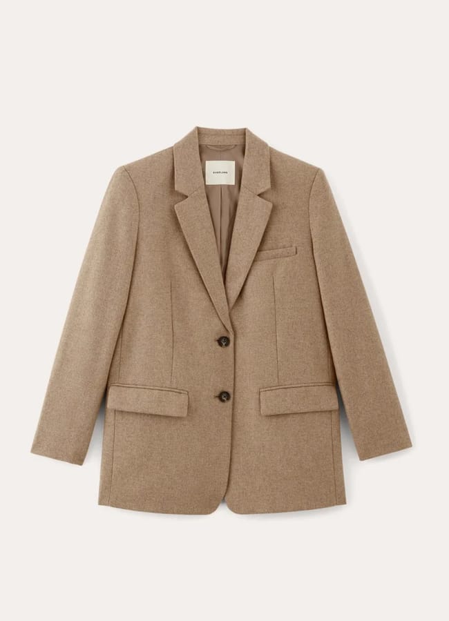 A tan wool blazer with a notched lapel, two front buttons, a chest pocket, and two flap pockets pairs effortlessly with track bottoms, displayed on a light background.