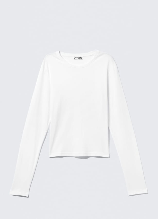 A plain white long-sleeve crop top with a round neckline, perfect for casual outfits, is laid flat against a light grey background.