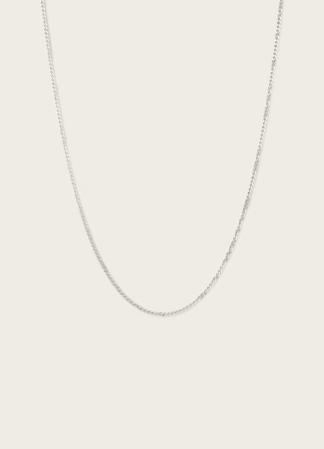 A thin, silver chain necklace displayed against a plain, light-coloured background—an effortless accessory perfect for men’s casual date night outfits.