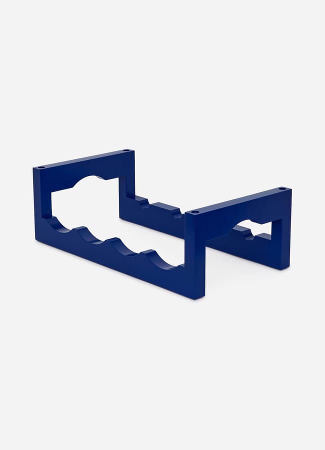 A blue plastic stand with grooves, designed to hold cylindrical objects such as bottles or rods, this practical high street homeware item is set against a plain white background.