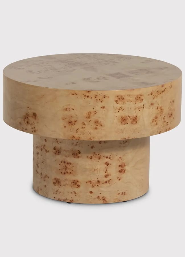 A modern round coffee table made of light-coloured wood with a distinctive burr pattern, featuring a thick circular top and a sturdy cylindrical base.
