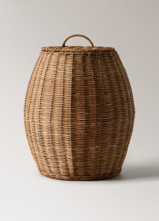 A large, rounded wicker basket with a woven lid and a small handle on top, this high street homeware piece is set against a plain, light background.