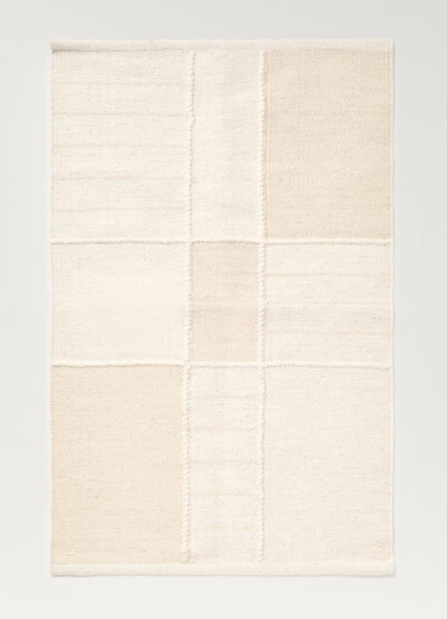 A rectangular rug with a patchwork design in neutral shades of cream and beige, inspired by high street homeware trends, featuring a grid of nine sections with subtle differences in texture and tone.