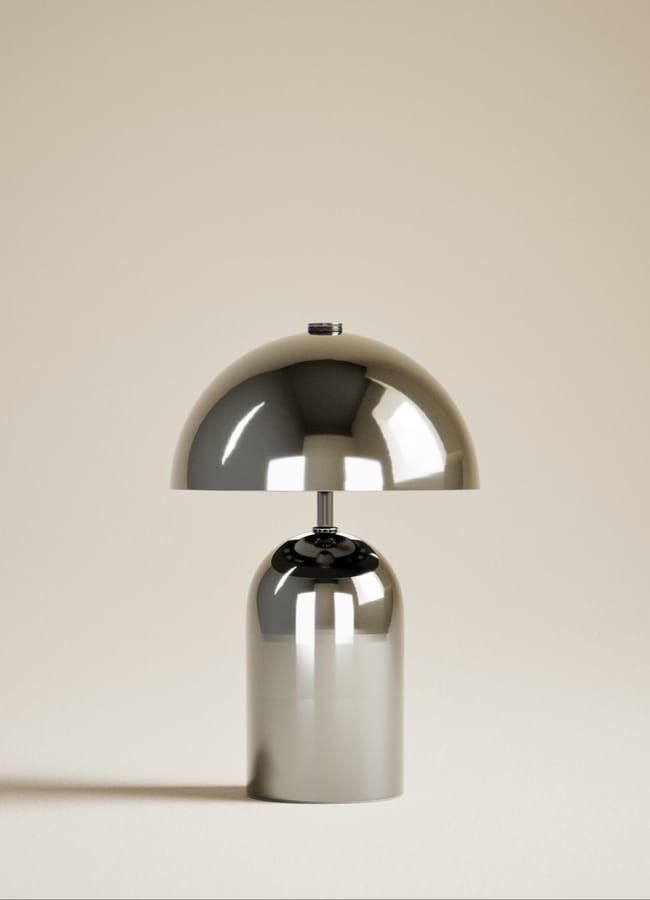 A modern, metallic table lamp with a shiny, dome-shaped shade and cylindrical base—an elegant addition to any high street homeware collection—set against a plain, beige background.