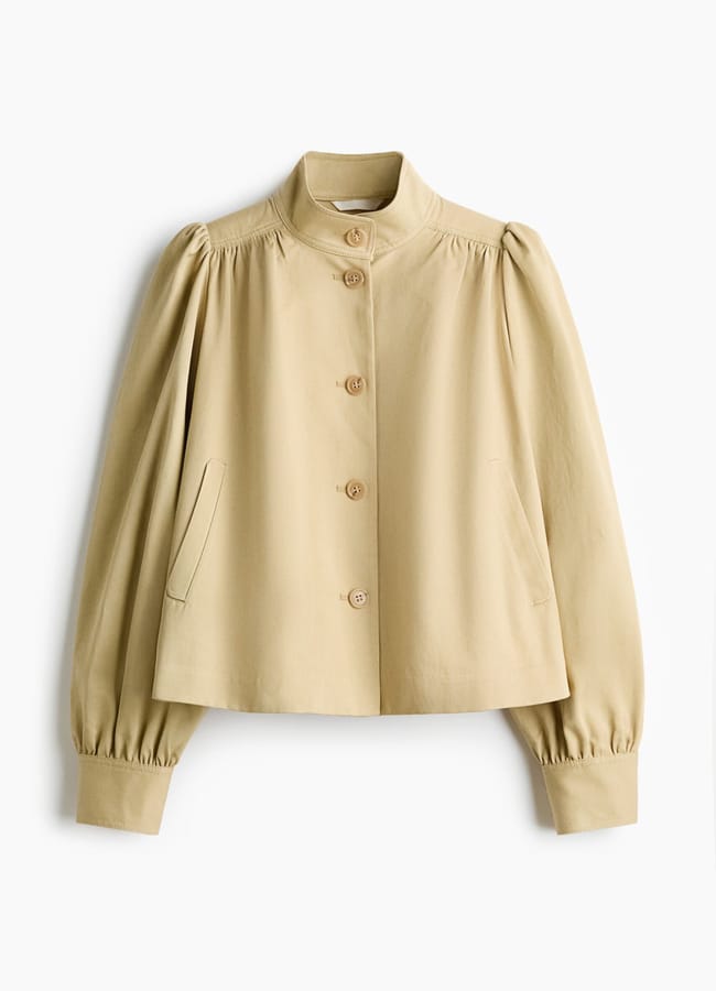 A light beige, cropped jacket from the H&M new season collection with a stand collar, button front, puffed long sleeves, and two slanted front pockets. Gathered details at the shoulders and cuffs add a stylish touch.