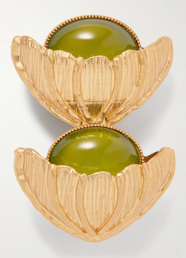A close-up of a gold-tone metal earring styled like two overlapping flower petals, each cradling a smooth, round green stone in the centre—a unique fashion accessory sure to elevate any look.