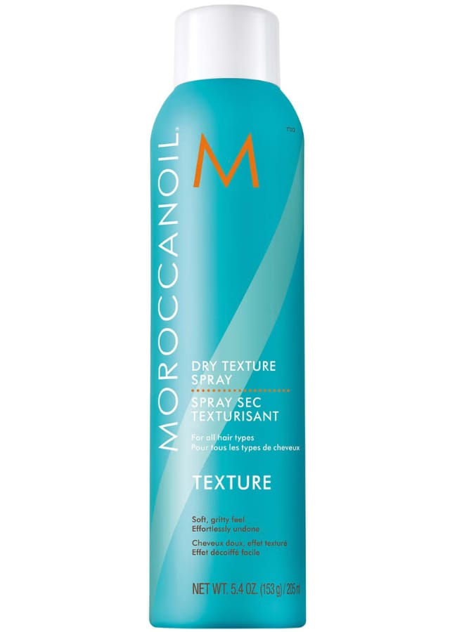 A turquoise can of Moroccanoil Dry Texture Spray with an orange M logo and white text, designed for all hair types—ideal for creating a Pamela Anderson mullet. 153 g (205 ml) size.