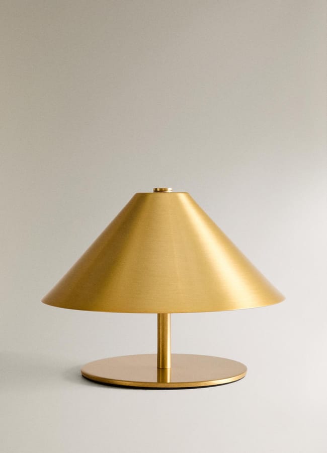 A modern gold table lamp with a wide, conical shade and a round base, set against a plain light grey background—an elegant addition inspired by high street homeware.