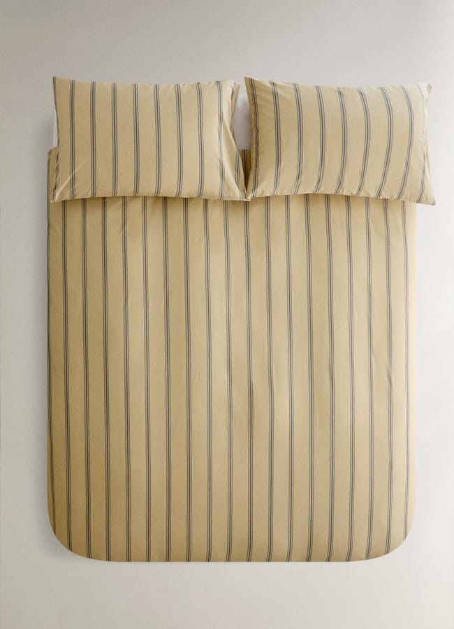 A neatly made bed with a beige duvet cover and matching pillowcases featuring vertical blue stripes, viewed from above against a light-coloured background, captures the timeless elegance of high street homeware.