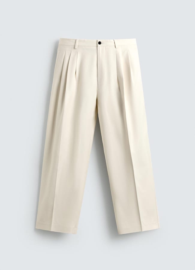Wide-leg, pleated beige trousers with belt loops and a button fastening, perfect for casual date night looks, laid flat on a light grey background.