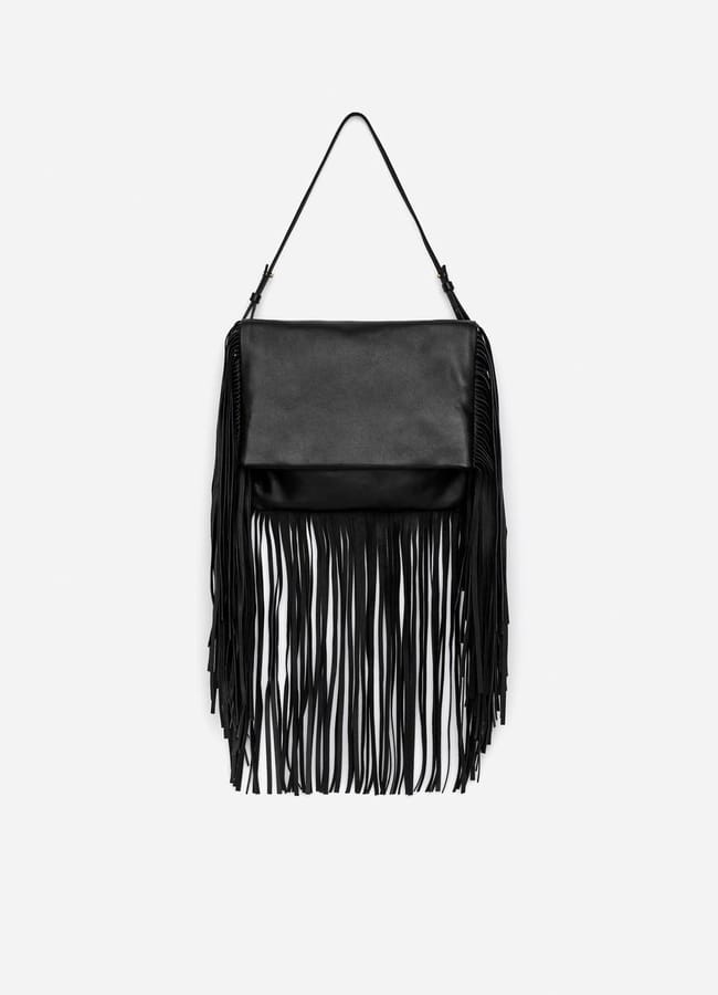 Black shoulder bag with long fringe detailing hanging from a single thin strap against a plain white background. This bag delivers serious fringe benefits with its rectangular shape and stylish flap fastening.
