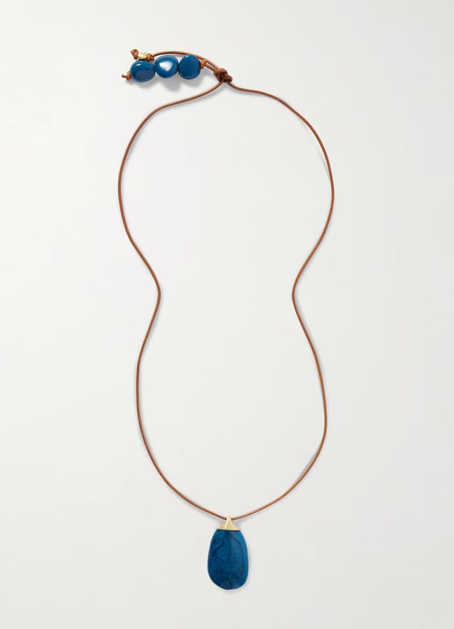 A long brown cord necklace with a sheer blue sculpted teardrop pendant and three round blue beads near the adjustable fastening.