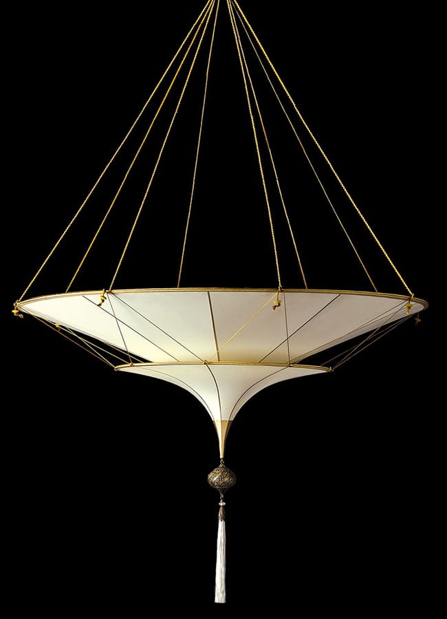 A modern, sculptural chandelier features two white, cone-shaped fabric layers suspended by gold cords with a decorative tassel, set against a black background—an Interiors Insider favourite.