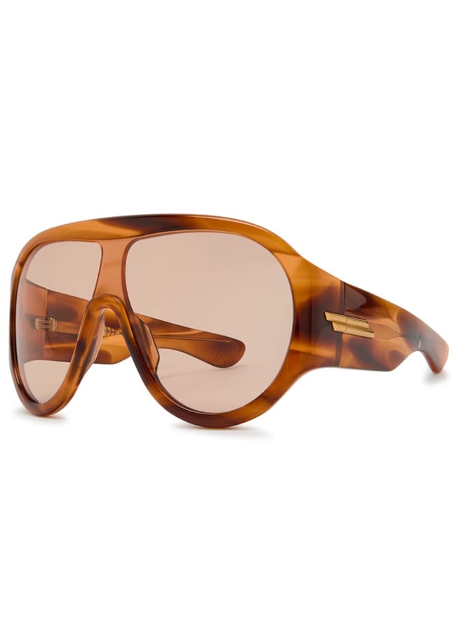 Oversized, brown tortoiseshell sunglasses with a wraparound design, thick frame, and large tinted lenses. The frame features a prominent brow bar and gold accents on the temples.