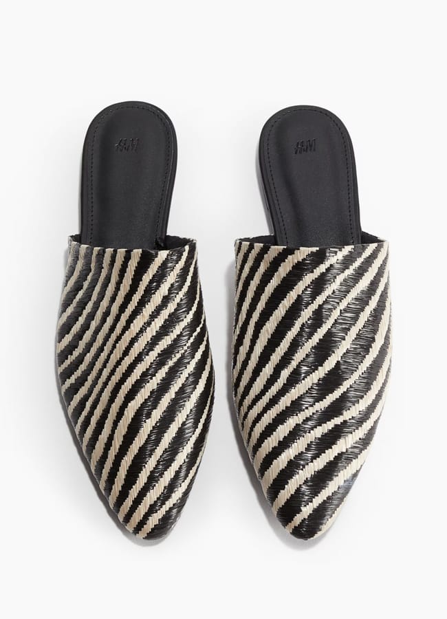 A pair of black and white slip-on mule shoes with a bold zebra print pattern and black insoles, seen from above.