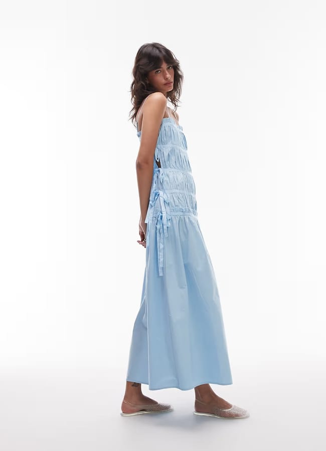 model standing to the side with arms behind her back wearing a topshop blue long ruched dress