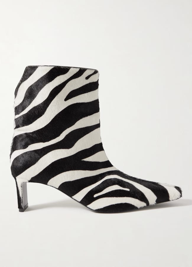 A pointed-toe ankle boot with a low heel, covered in bold zebra print, stands out in striking black and white against a plain white background.