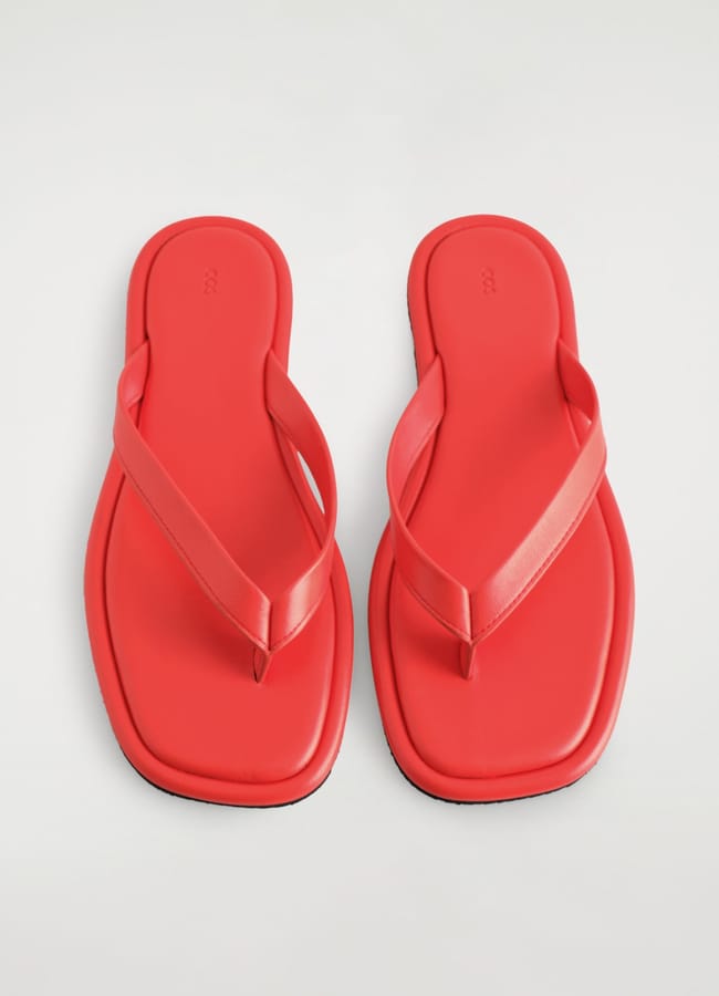 A pair of bright red flip-flop sandals with wide straps and square-shaped soles, displayed on a plain white background.