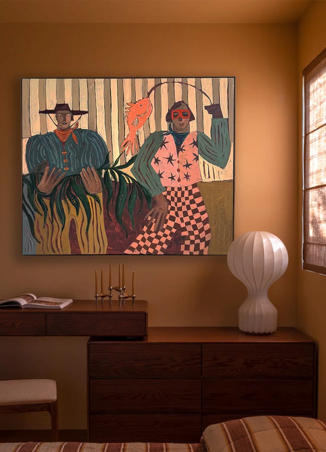 A cosy, warmly lit room by Interiors Insider Lucy Barlow features beige walls, a modern wooden desk, an open book, a white sculptural lamp, and a vibrant painting above—sunlight streams through the window blind.