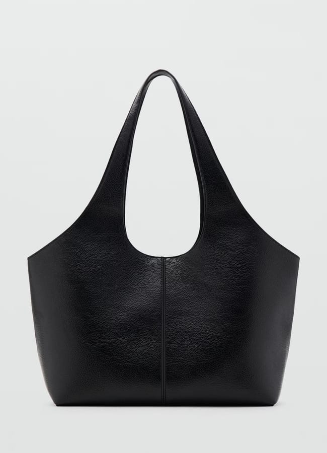 A large black leather tote bag, embodying the understated elegance of big bags, with a wide, rounded base and two elongated handles, is photographed against a plain light grey background.