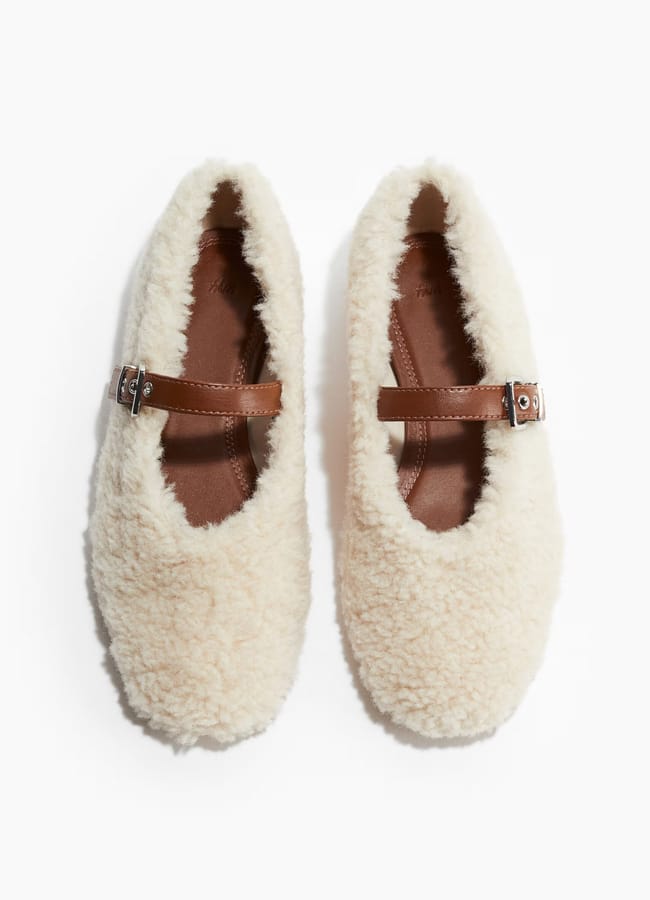A pair of cream-coloured, fuzzy Mary Jane shoes with brown straps and silver buckles—perfect for recreating your favourite looks or adding a cosy touch to any wardrobe, displayed on a white background.