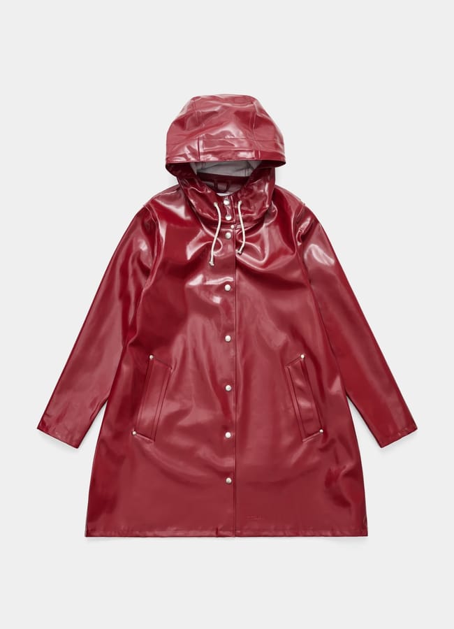 A shiny, dark red raincoat with a hood, front press studs, white drawstrings, and two slanted front pockets—one of our stylish waterproof jackets—is laid flat on a plain, light background.