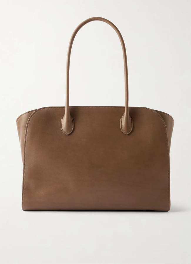 A large brown leather tote bag with two long handles, simple stitching, and a minimalist, structured design epitomises the appeal of big bags, displayed against a plain white background.
