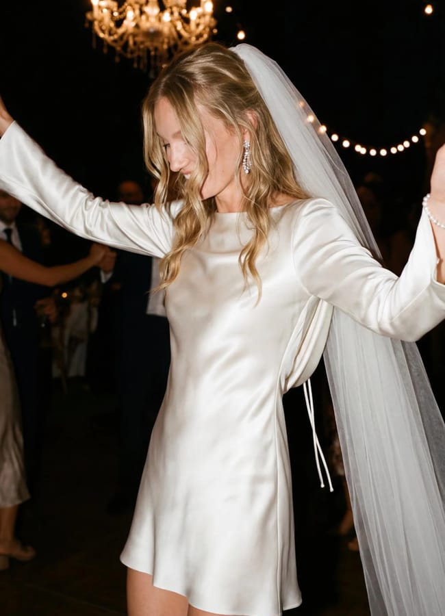bride at wedding party dancing with hands in the air wearing a veil and 100% Silk mini dress