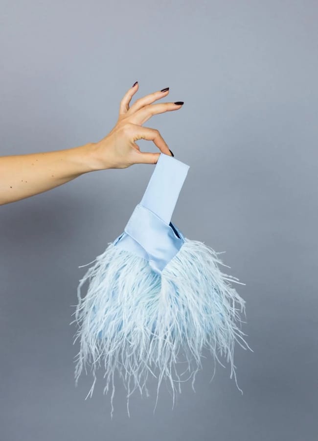 hand holding pale blue japanese knot bag trimmed with feathers