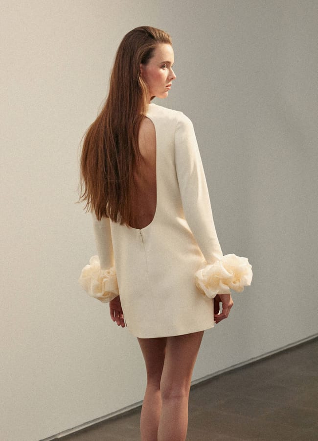 model standing with back to the camera wearing white Open-back dress with flower cuffs