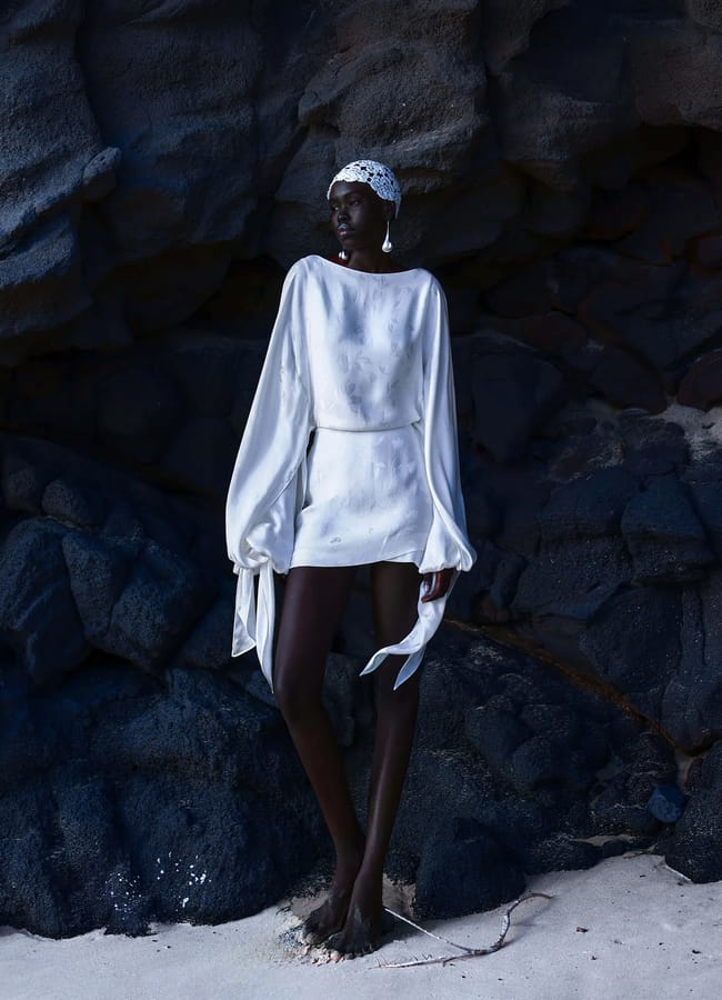 model on beach against dark rocks wearing Rat SISLEY DRESS in white