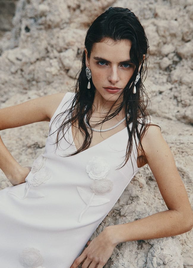 model laying on rocks wearing Appliquéd embellished crepe mini dress in white