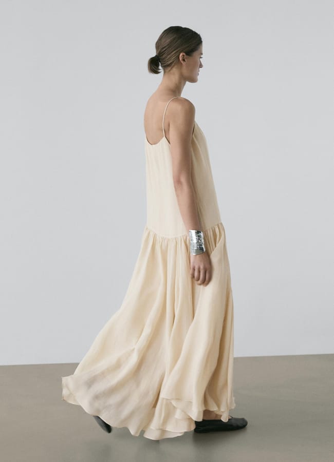 model turned to side with back to camera wearing md Flowing midi dress with pleated detail in cream