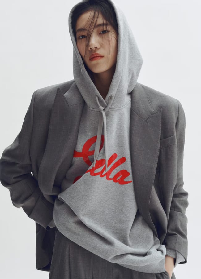 model wearing grey hodie with red stella writing on it and blazer