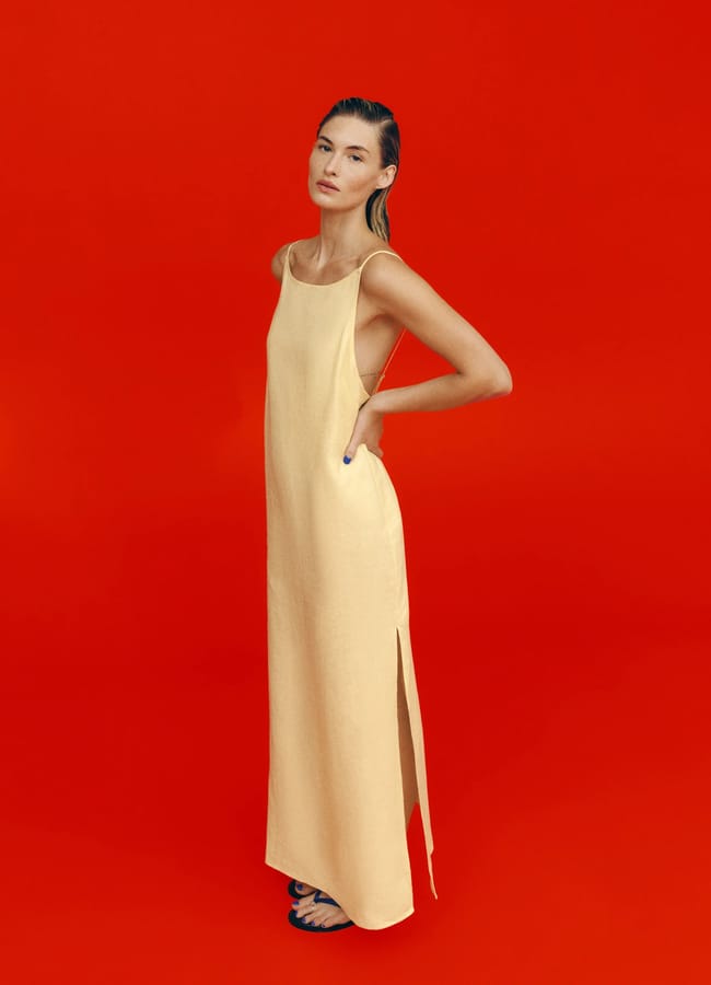 model wearing yellow column style maxi Serena Linen Dress on red background