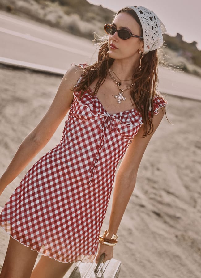 model on sandy road wearing red and white plaid mini dress, sunglasses and headscarf